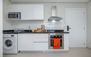 Cuina compacta amb rentadora, microones, forn i campana extractora d'acer inoxidable.