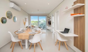 A modern dining area with a long table, white chairs, and a laptop on a desk.