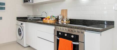 A modern kitchen with a built-in washing machine, a microwave, an oven, and a stainless steel range hood.
