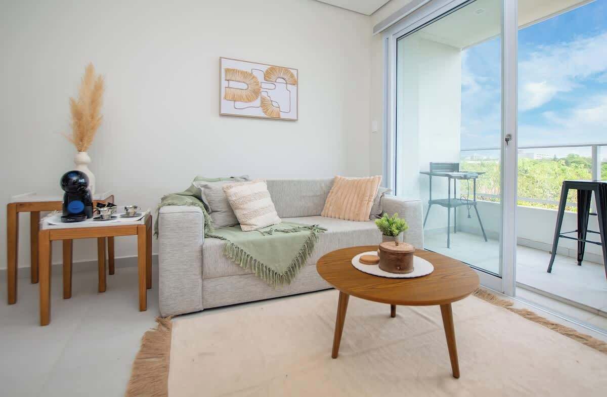 A modern living room with a grey sofa, a wooden coffee table, a small side table with a vase, and a balcony with a glass door.