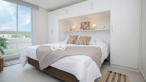 A bedroom with a large bed, white cabinets, a window, and a view of the outside. - Corporate Stays First Living - 306 (Asunción)