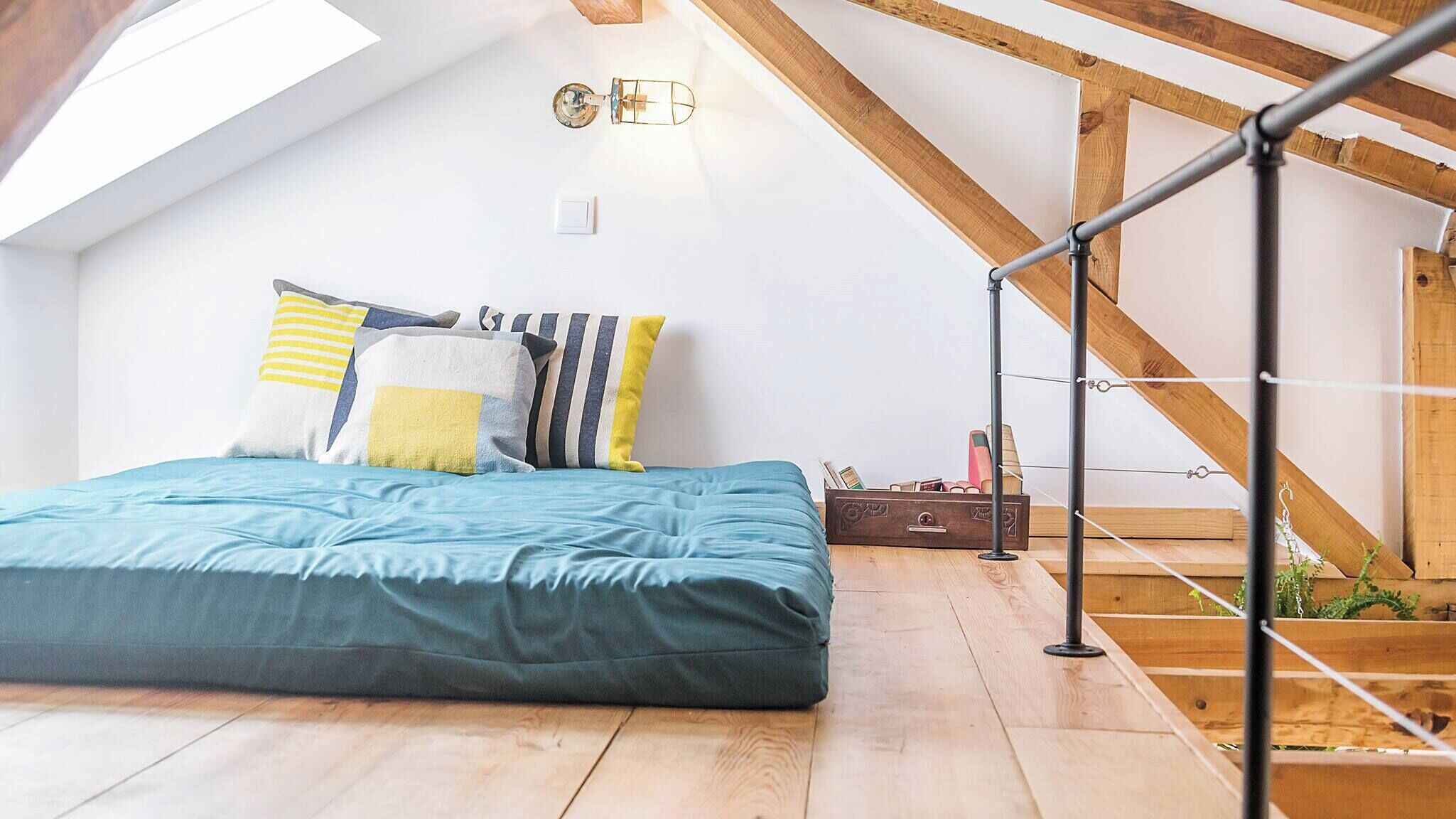 An attic bedroom with a sloped ceiling, a bed with a blue bedspread, striped pillows, and a small wooden chest of drawers.