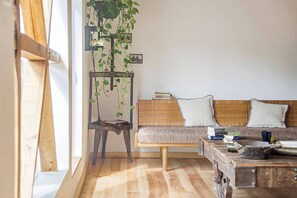 Una habitació amb sòl de fusta, un sofà amb coixins, una taula de cafè, una planta penjant i una prestatgeria.
