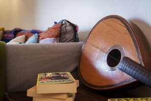 Une guitare appuyée contre un mur, un livre intitulé « A SEVERA » sur une table, et un canapé agrémenté de coussins colorés.
