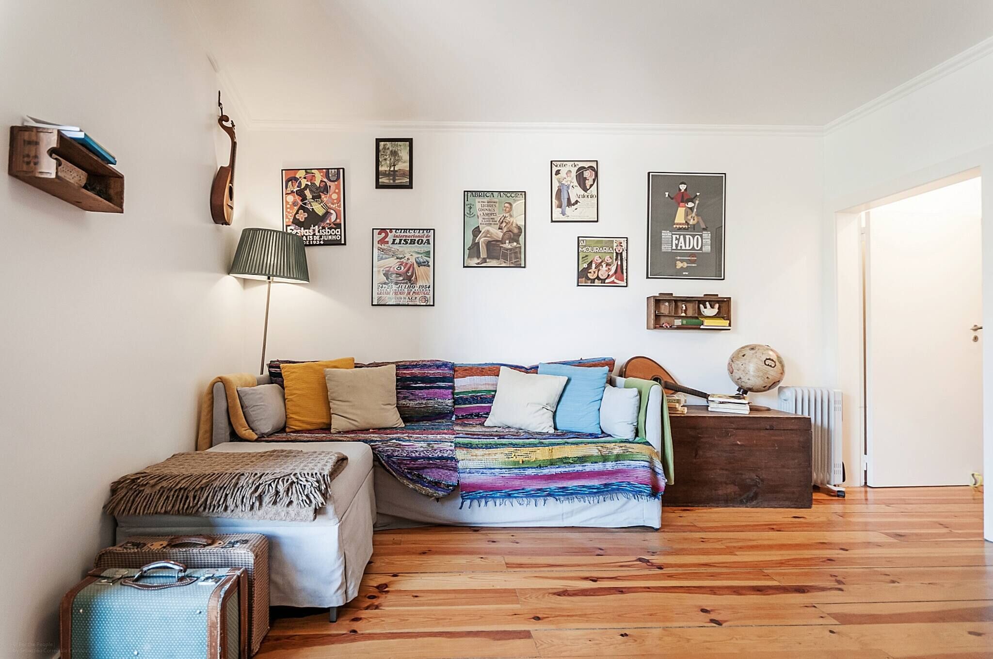 A cozy bedroom with a bed, a lamp, a guitar, and various framed pictures on the wall.