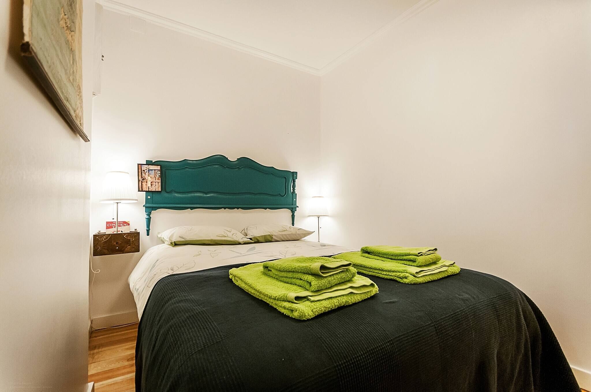 A bed with a teal headboard, white bedding, and green towels.