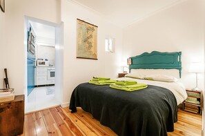 A bedroom with a bed, a map on the wall, a nightstand with books, and a view into the kitchen. - Charming Mouraria Apartment With Private Terrace in Lisbon (Lisbon)