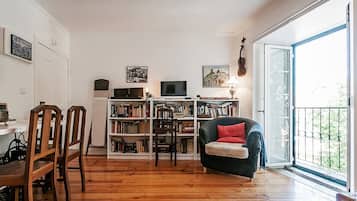 A living room with a wooden floor, a bookshelf, a television, and a window with a view.