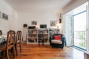 A living room with a wooden floor, a bookshelf, a television, and a window with a view. - Charming Mouraria Apartment With Private Terrace in Lisbon (Lisbon)