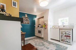 A compact kitchen with a microwave, oven, and sink. There is a patterned rug on the floor and a small table with a chair. - Charming Mouraria Apartment With Private Terrace in Lisbon (Lisbon)