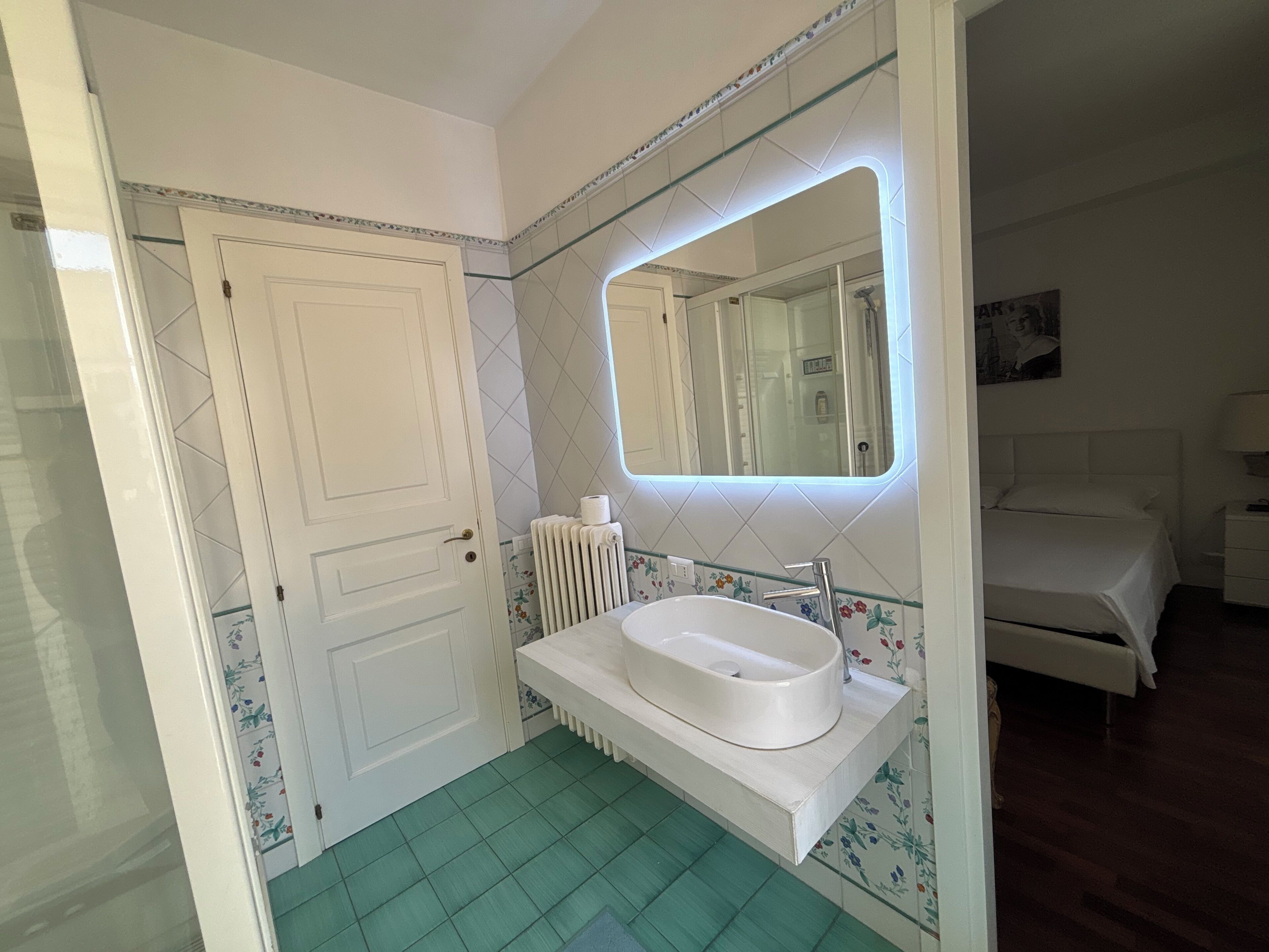 A bathroom with a white sink, a mirror, a radiator, and a door.