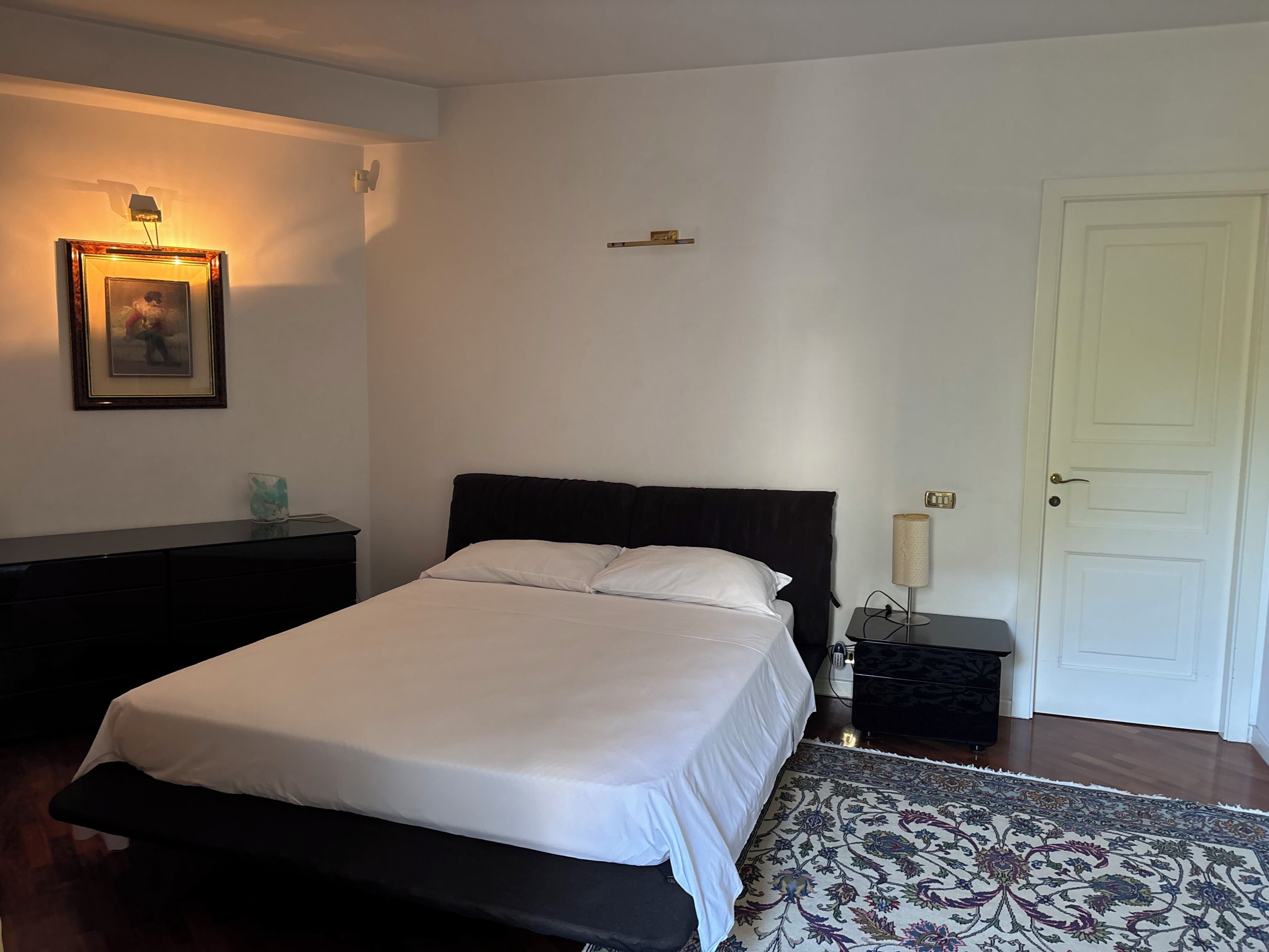 A bedroom with a bed, bedside tables, a lamp, a door, and a framed picture on the wall.