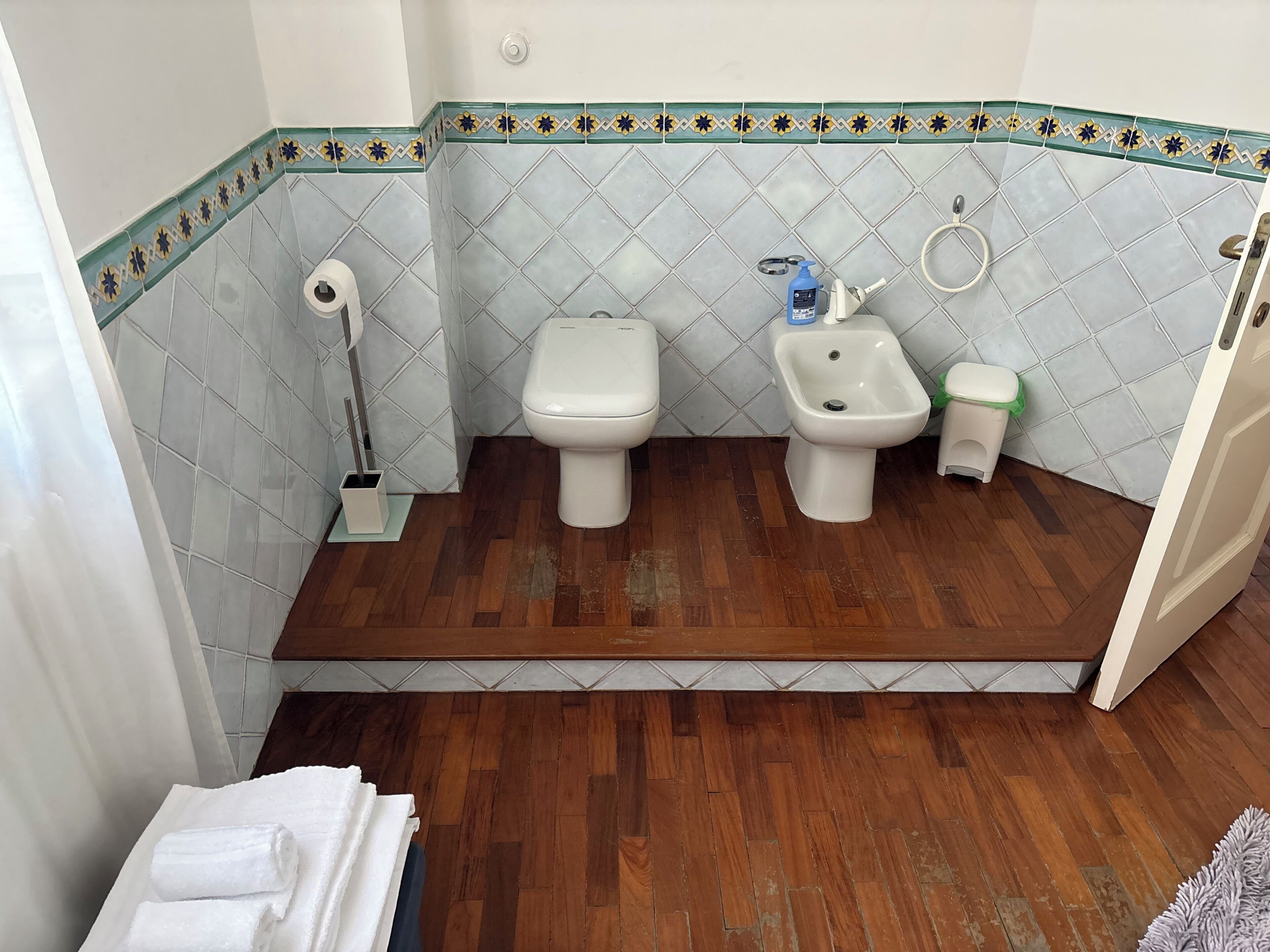 Une salle de bain comprenant des toilettes, un bidet et un lavabo, avec un plancher en bois et des carreaux décoratifs.