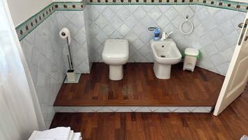 Une salle de bain comprenant des toilettes, un bidet et un lavabo, avec un plancher en bois et des carreaux décoratifs.