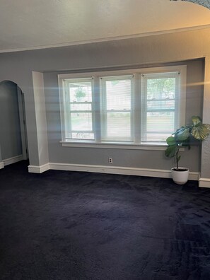 A room with a dark carpet, a large window with blinds, and a potted plant. - Charming 2-bedroom house in Milwaukee perfect for commercial or business use (Milwaukee)