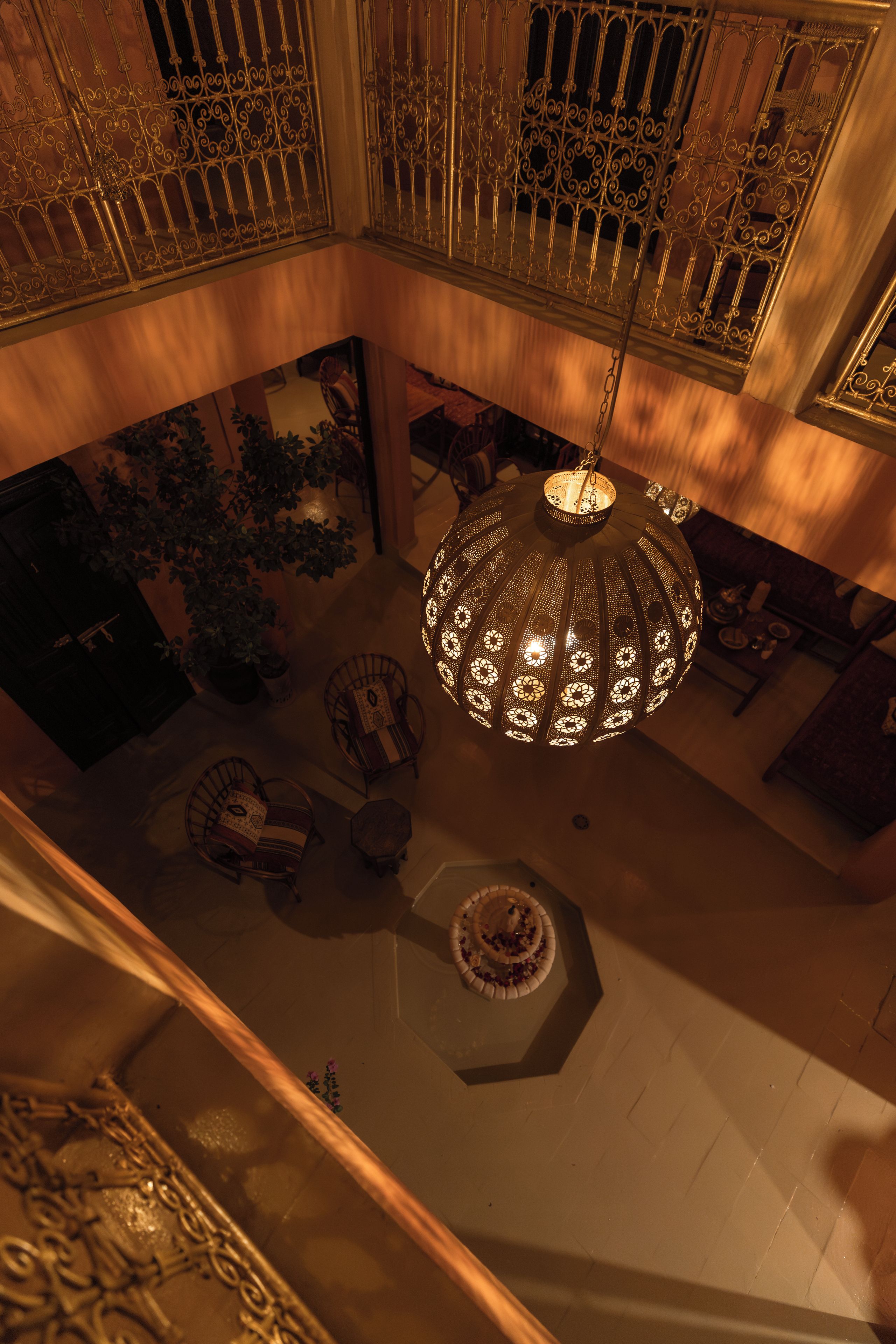 A high-ceilinged room with ornate metal railings, a central chandelier, and a seating area with patterned cushions.