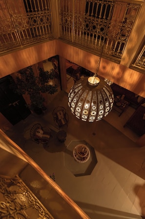 A high-ceilinged room with ornate metal railings, a central chandelier, and a seating area with patterned cushions.