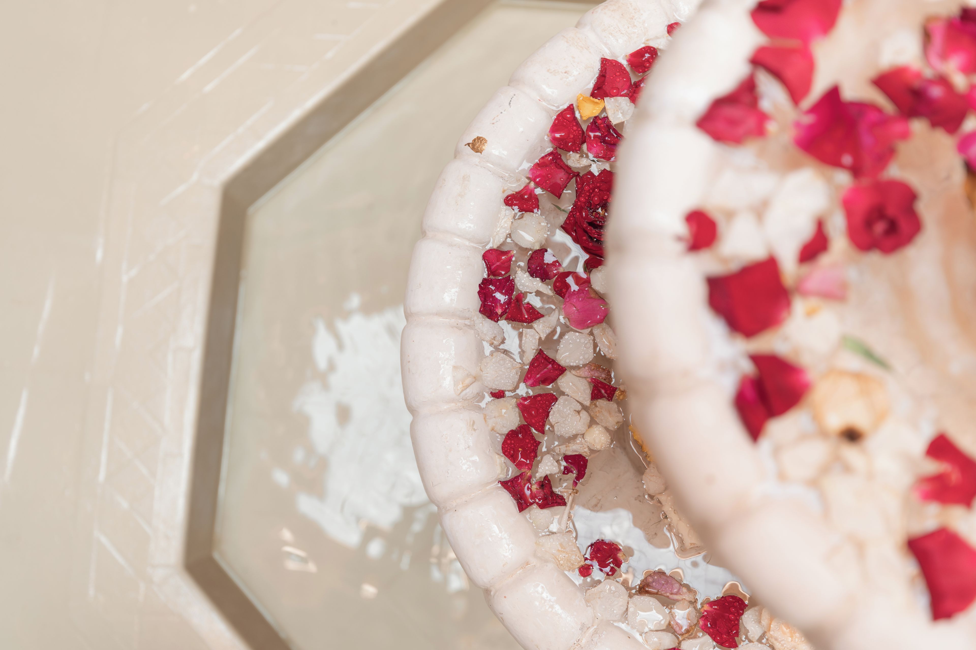 A bathtub with rose petals and white stones.