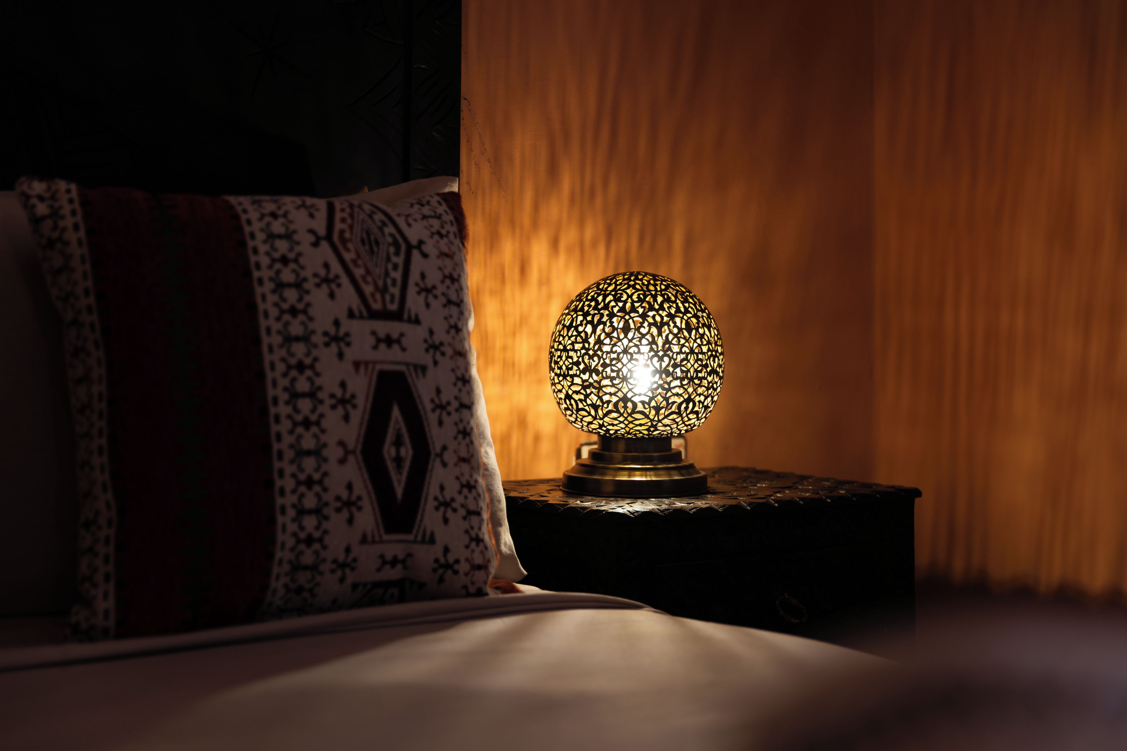 Un lit avec un oreiller à motifs et une lampe décorative sur une table de chevet.