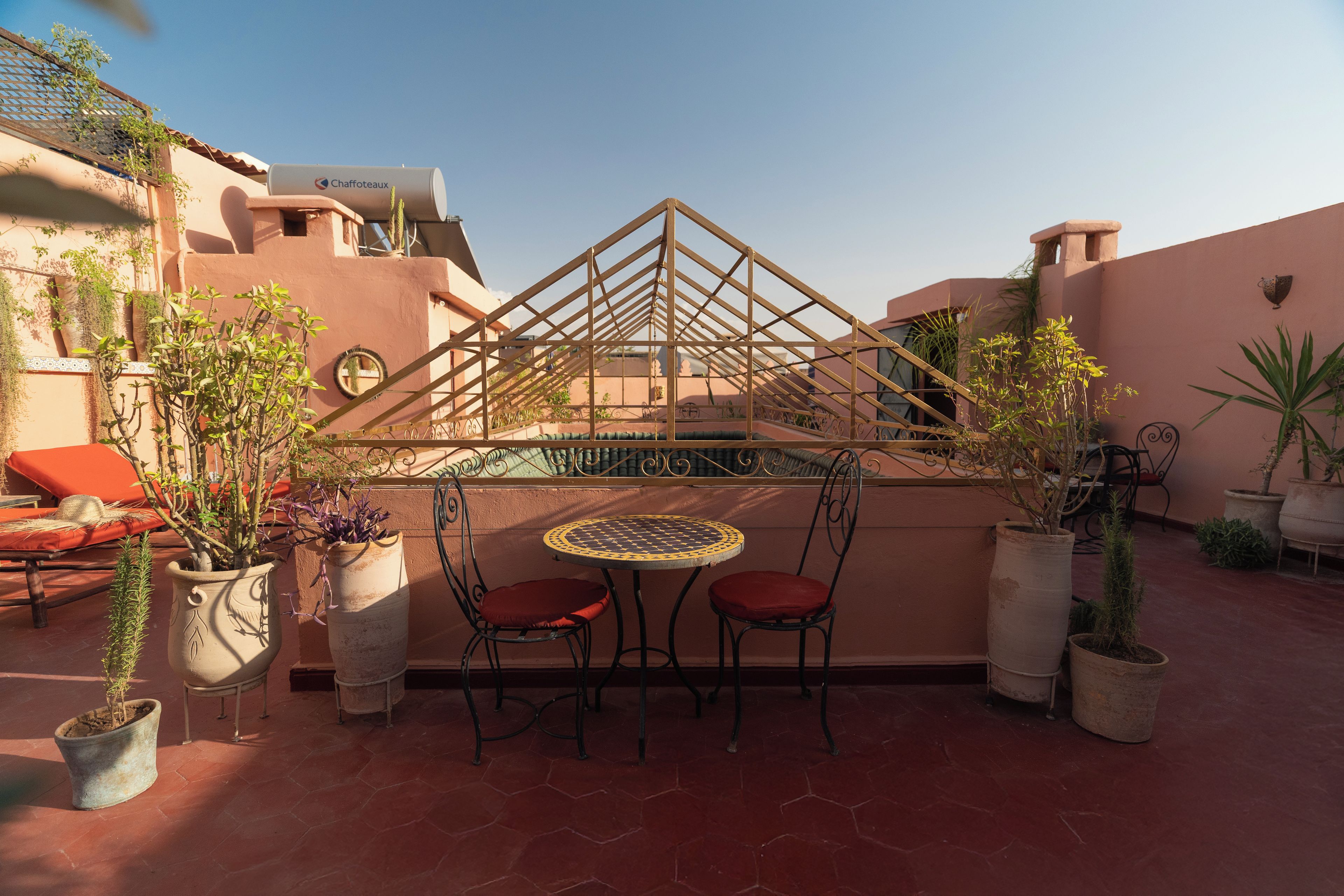 A rooftop terrace with a table and chairs, potted plants, and a view of the cityscape.