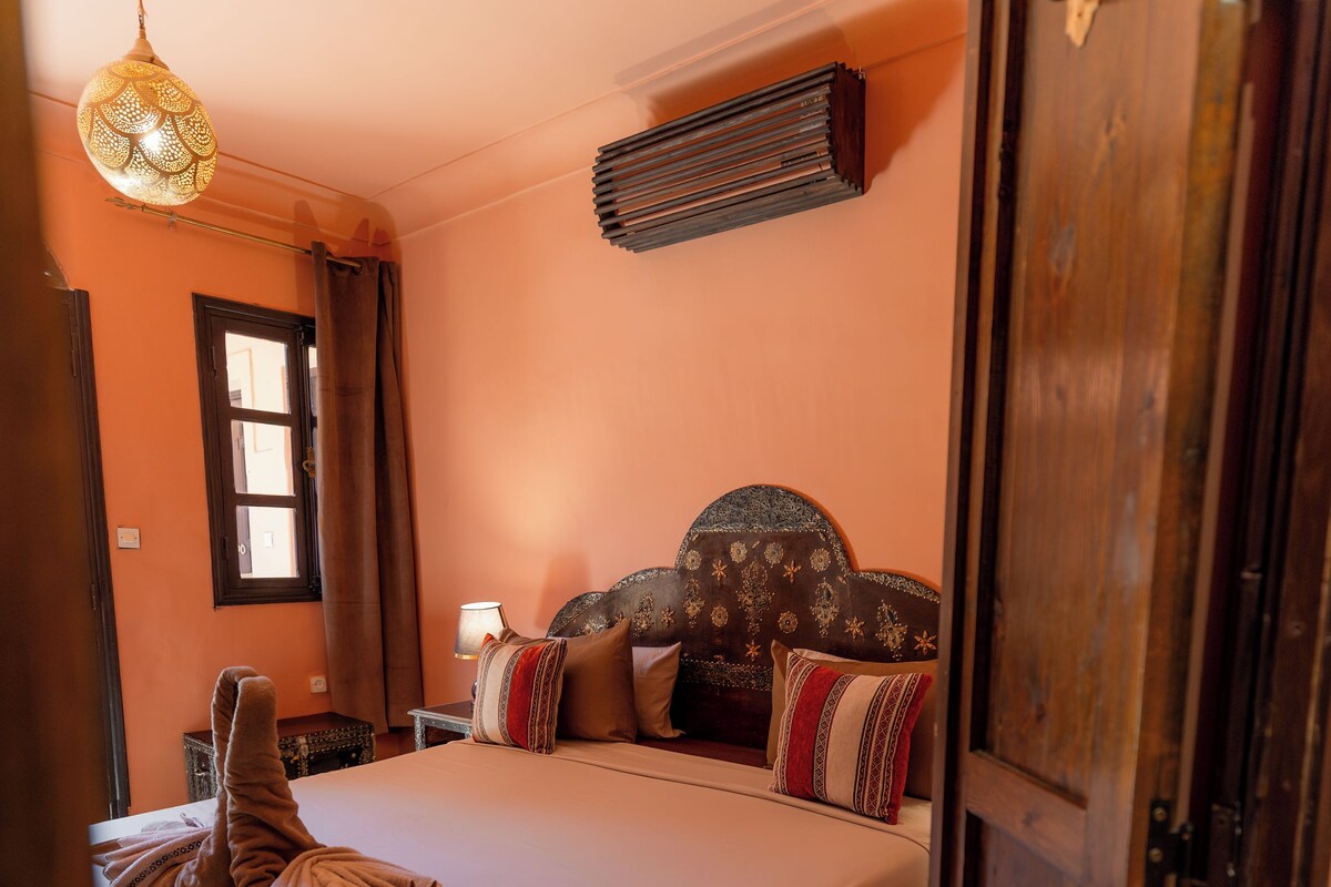 A bedroom with a bed, a bedside table, a lamp, a hanging light fixture, and a wardrobe.