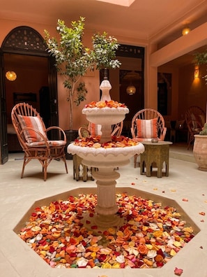A multi-tiered fountain surrounded by chairs and a table, with scattered flower petals on the floor.