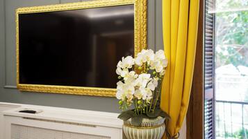 A room with a large framed television, a radiator, and a vase with white flowers.