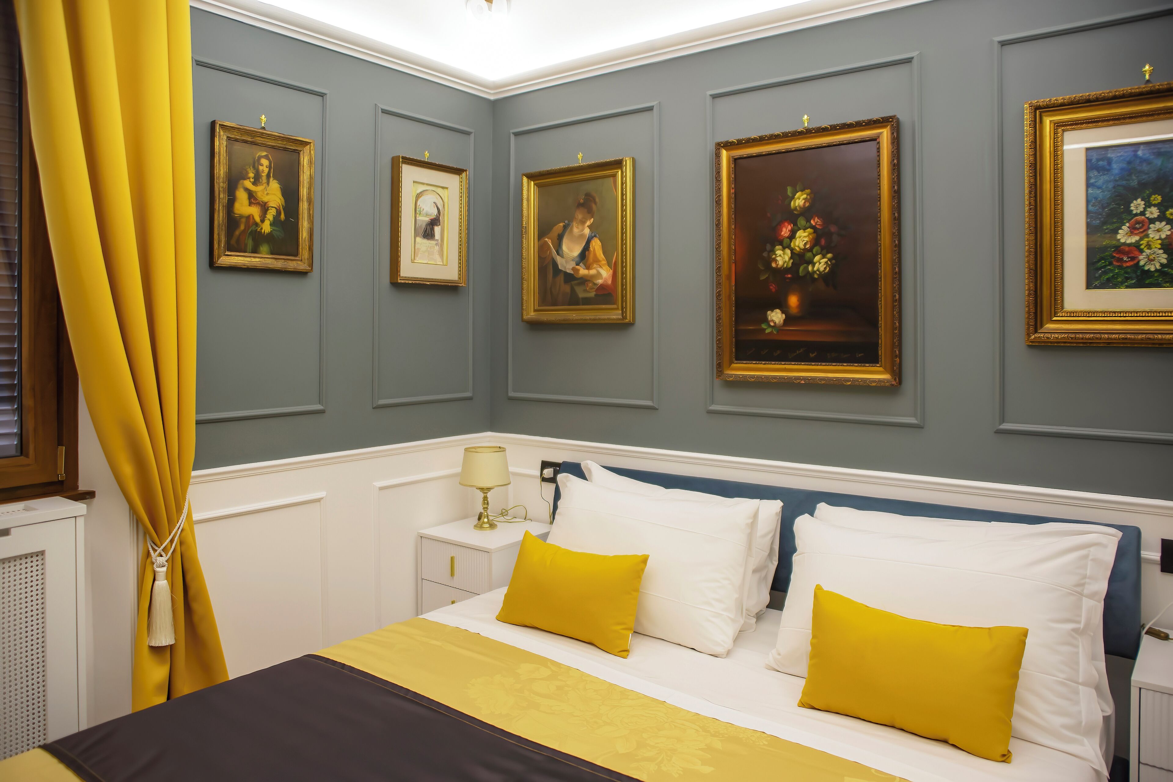 Habitación de hotel con cama, mesita de noche, lámpara y cuadros colgados en la pared.