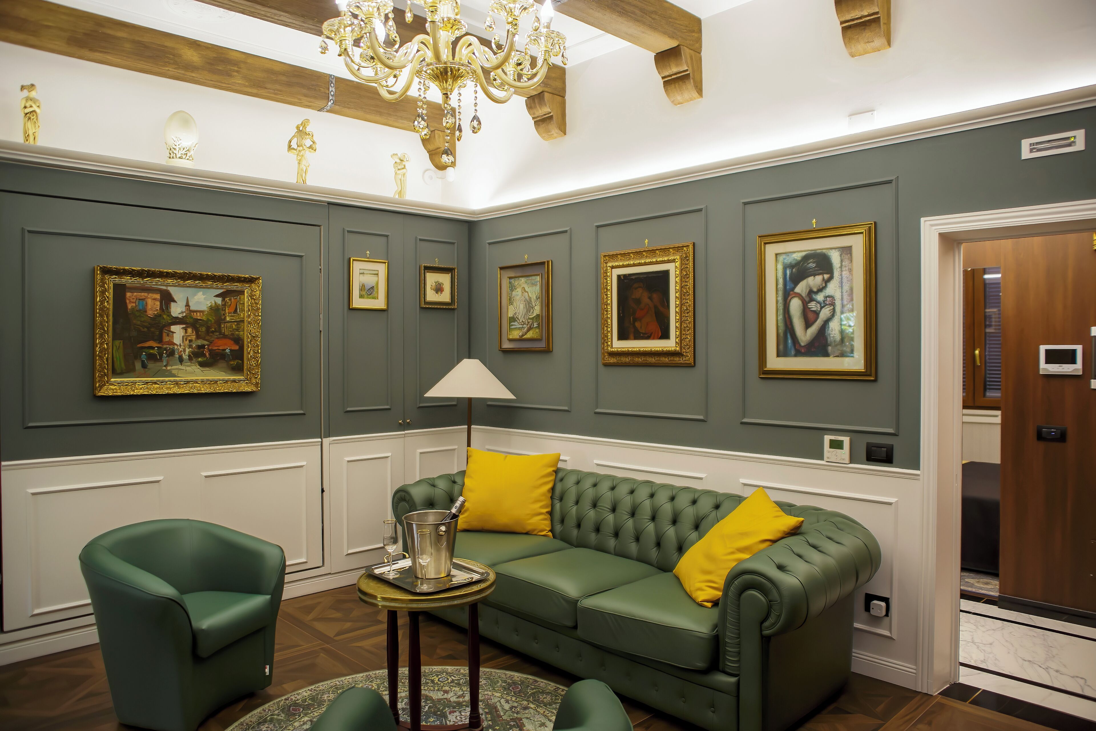 Una habitación con un sofá verde, un sillón verde, una mesita redonda con una lámpara y un candelabro.
