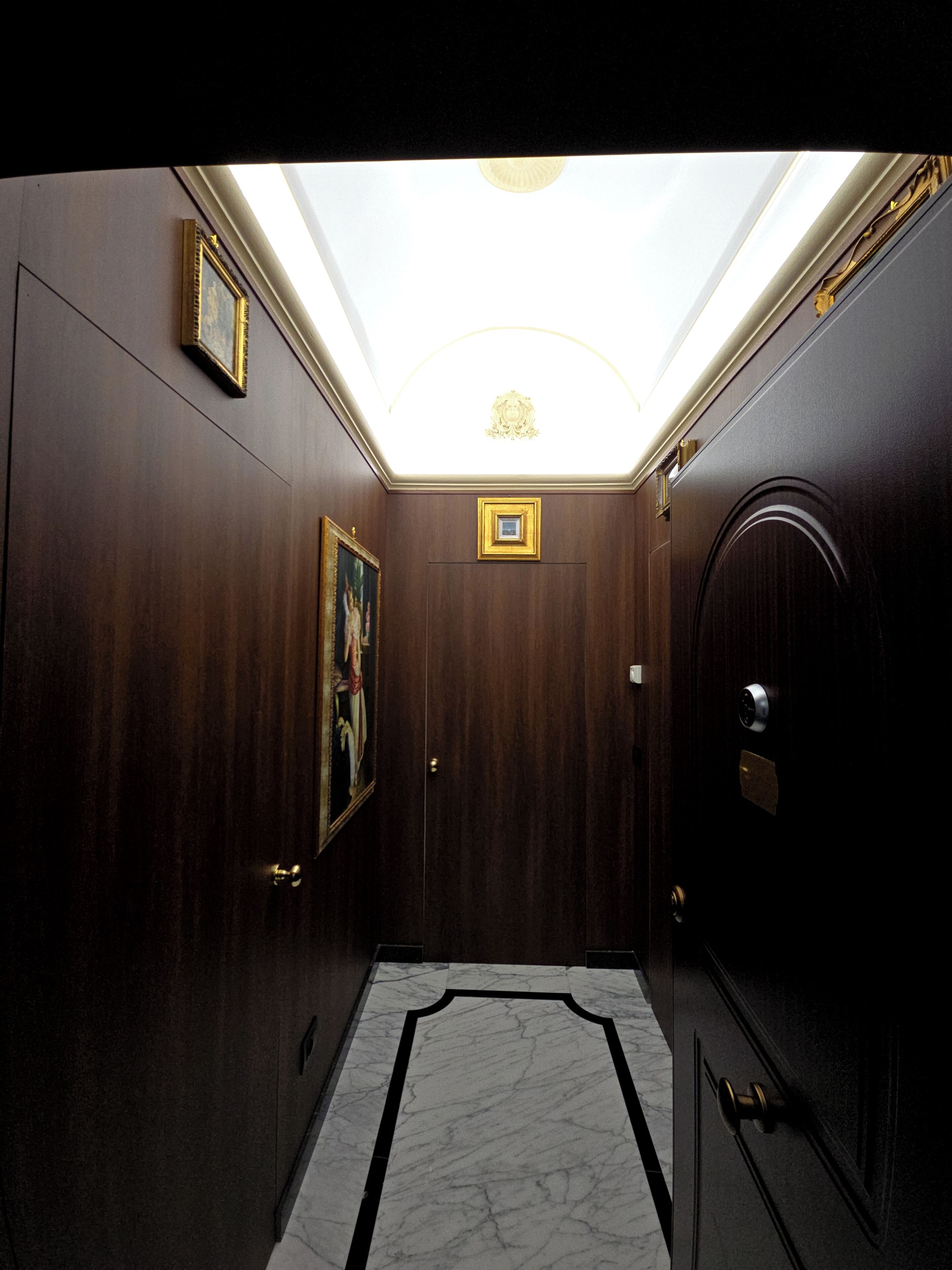 A hallway with a marble floor, wooden walls, a framed picture, and a ceiling light.