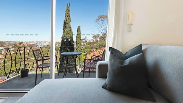 En balkon med sofa og stole, et bord samt udsigt over bybilledet.