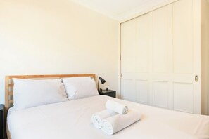 A hotel room with a bed, a nightstand, a lamp, and a closed door. - Penthouse with Harbour Views in Neutral Bay (Neutral Bay)