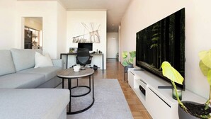 En moderne stue med en grå sofa, et rundt sofabord, et fladskærms-tv og en stor plante.