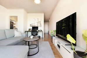 A modern living room with a grey sofa, a round coffee table, a flat-screen TV, and a large plant. - Penthouse with Harbour Views in Neutral Bay (Neutral Bay)
