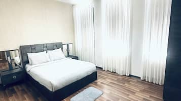 Un dormitorio con cama, mesitas de noche, una lámpara, luz de techo, ventana con cortinas y suelo de madera.