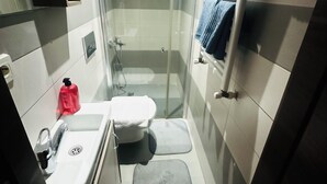 Casa de banho compacta com sanita, lavatório e chuveiro.
