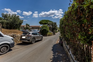 Una strada stretta con auto parcheggiate e un edificio con tetto rosso sullo sfondo.