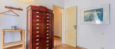 Un pasillo con un aparador de madera, un estante de bambú, una lámpara colgante, una puerta y un cuadro en la pared.