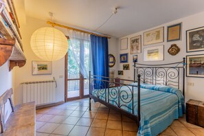 A bedroom with a bed, a radiator, a window with curtains, and wall-mounted pictures.