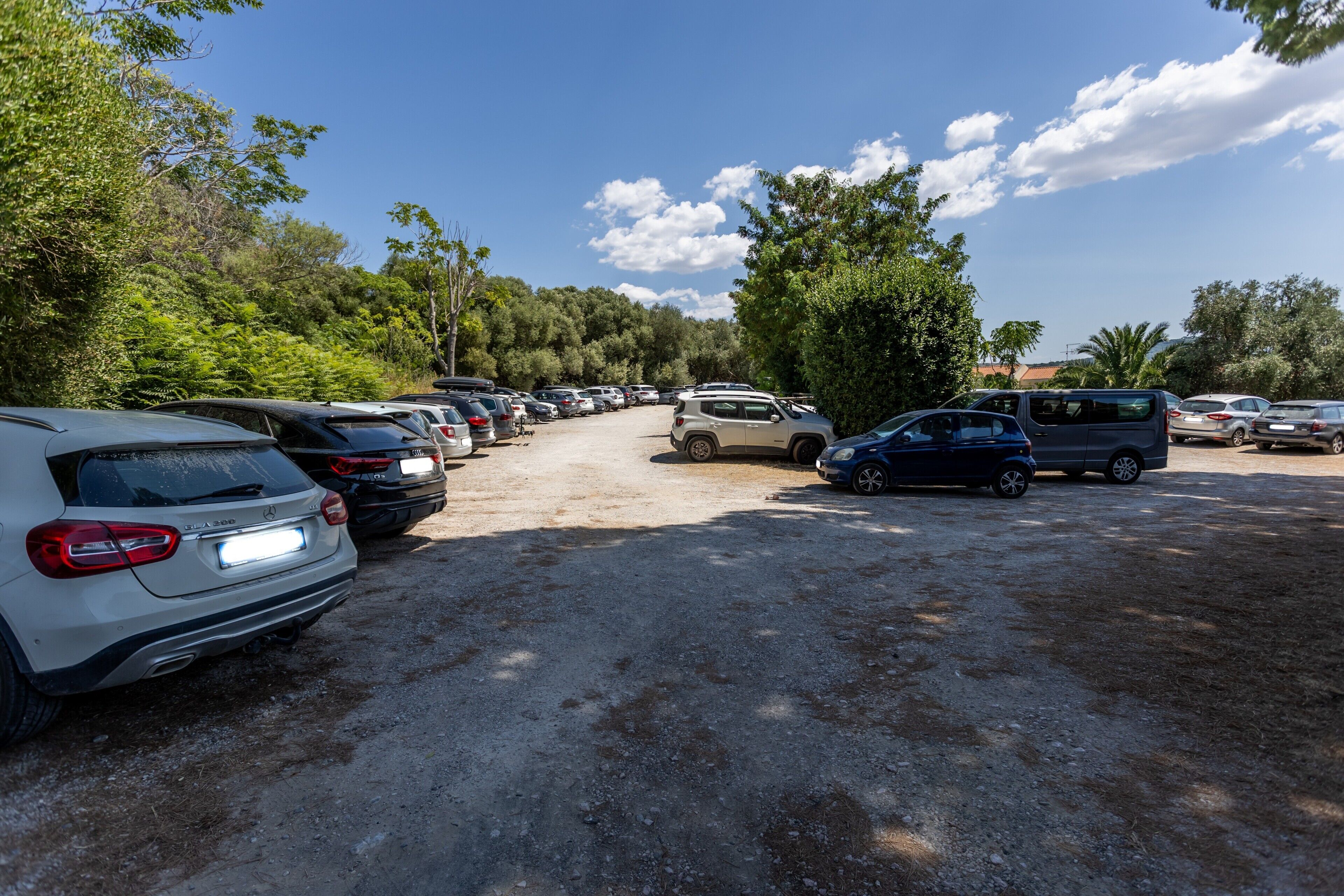 A parking lot with various cars and a dirt path leading to a building.