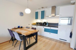A compact kitchen with a wooden table and chairs, a built-in oven, and a coffee maker. - Modern apartment for up to 4 guests beside the dunes of Callantsoog. Enjoy a terrace with dune views, a luxury bathroom with shower and bathtub, and two bedrooms, including one with a double sofa bed. (Callantsoog)