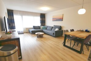 Ein Wohnzimmer mit Sofa, Couchtisch, Esstisch und einem Mülleimer.