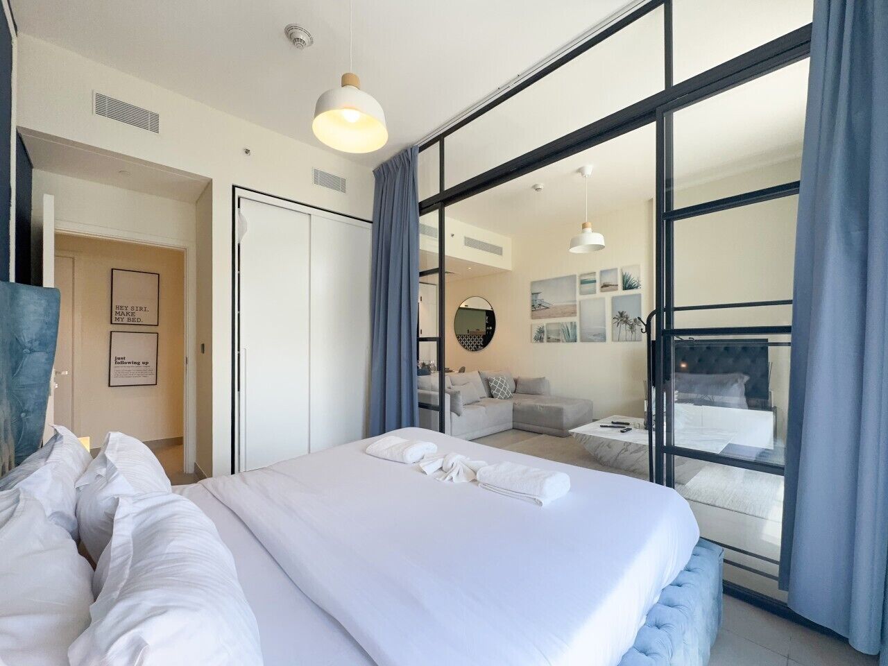 Habitació d'hotel moderna amb un llit gran, un sofà, zona de dinar i vista a través d'una porta de vidre.