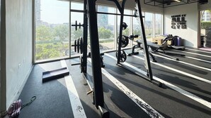 Uma academia com equipamentos de musculação, esteira e uma grande janela com vista para a cidade.