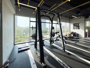 Ein Fitnessraum mit Krafttrainingsgeräten, einem Laufband und einem großen Fenster mit Blick auf die Stadt.