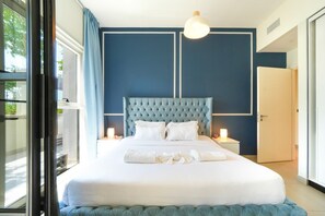 Ein Schlafzimmer mit einem großen Bett, einem gebürsteten Kopfende, Nachttischlampen und Blick durch ein Fenster.