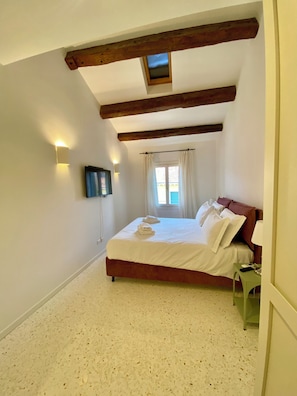 A bedroom with a bed, a TV, a window with curtains, and a small table. - Apartment with a view of the canal in a Venetian building (Venezia)