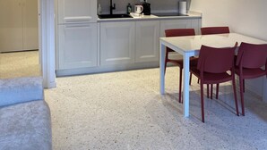 A compact kitchen with white cabinets, a red microwave, and a dining table with red chairs. - Apartment with a view of the canal in a Venetian building (Venezia)