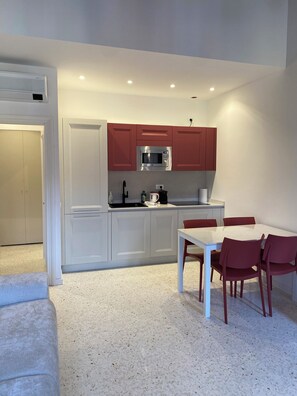 A compact kitchen with white cabinets, a red microwave, and a dining table with red chairs. - Apartment with a view of the canal in a Venetian building (Venezia)