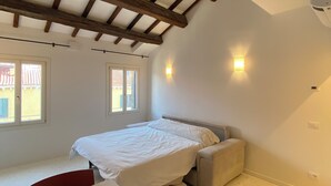 A bedroom with a bed, a desk, and a chair. There are windows and a ceiling with wooden beams. - Apartment with a view of the canal in a Venetian building (Venezia)